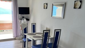 A dining area with a white table and blue chairs, a flat-screen TV, and a large window with a view.