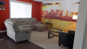 A living room with a sectional sofa, a glass coffee table, and a red accent wall.