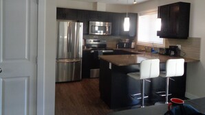 A modern kitchen with stainless steel appliances, a central island with bar stools, and a window with blinds.