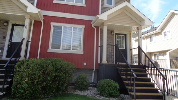 A two-story residential building with a red facade, white trim, and a small front porch with steps leading to the entrance.