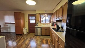 Una cocina con gabinetes de madera, lavavajillas de acero inoxidable, refrigerador negro y ventana con vista al exterior.