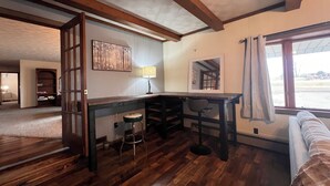 Una habitación acogedora con pisos de madera, un escritorio, una silla y un ventanal con cortinas.