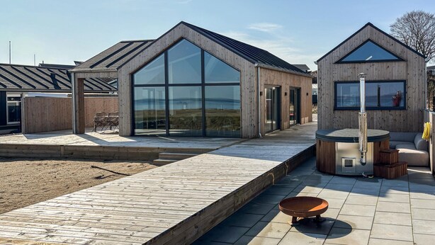 Una casa moderna con amplios ventanales, una terraza de madera y un jacuzzi.