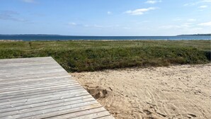 Un muelle de madera que conduce a una playa de arena, con un área cubierta de césped y vistas al océano.