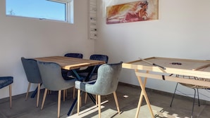 Un comedor con una mesa de madera y sillas tapizadas en azul, un cuadro en la pared y una ventana con persianas.