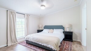 Een slaapkamer met een bed, twee nachtkastjes met lampen, een raam met gordijnen en een kamerkleed met een patroon.