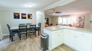 Een moderne keuken met witte kasten, een eethoek met tafel en stoelen, en een woonkamer met een bank en televisie.