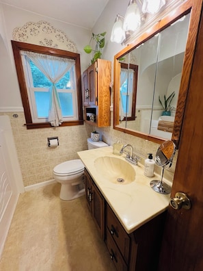 Un baño con inodoro, lavamanos, espejo y ventana con cortinas.