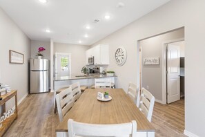 Una cocina moderna con armarios blancos, un refrigerador de acero inoxidable y una mesa de comedor de madera con sillas blancas.