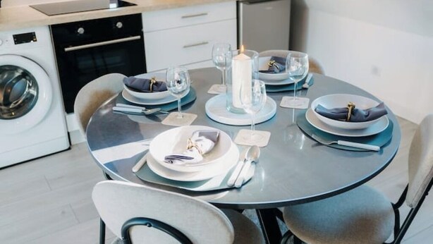 A modern kitchen with a round dining table set for four, featuring white plates, blue napkins, and clear glassware. - Sewwa - In the heart of Alsace at Sélestat (Sélestat)