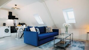 A modern loft apartment with a blue sofa, a glass coffee table, and a kitchen area. - Sewwa - In the heart of Alsace at Sélestat (Sélestat)