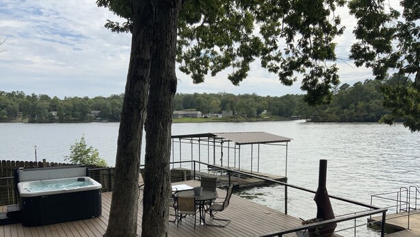Une terrasse en bois avec un jacuzzi, un espace salon extérieur et une vue sur un lac.