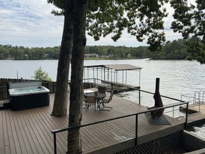 A wooden deck with a hot tub, outdoor seating, and a view of a lake.