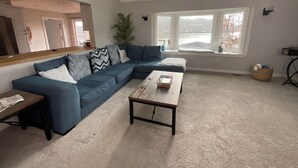 Un salon moderne avec un canapé d’angle, une table basse et une grande fenêtre offrant une vue sur l’extérieur.