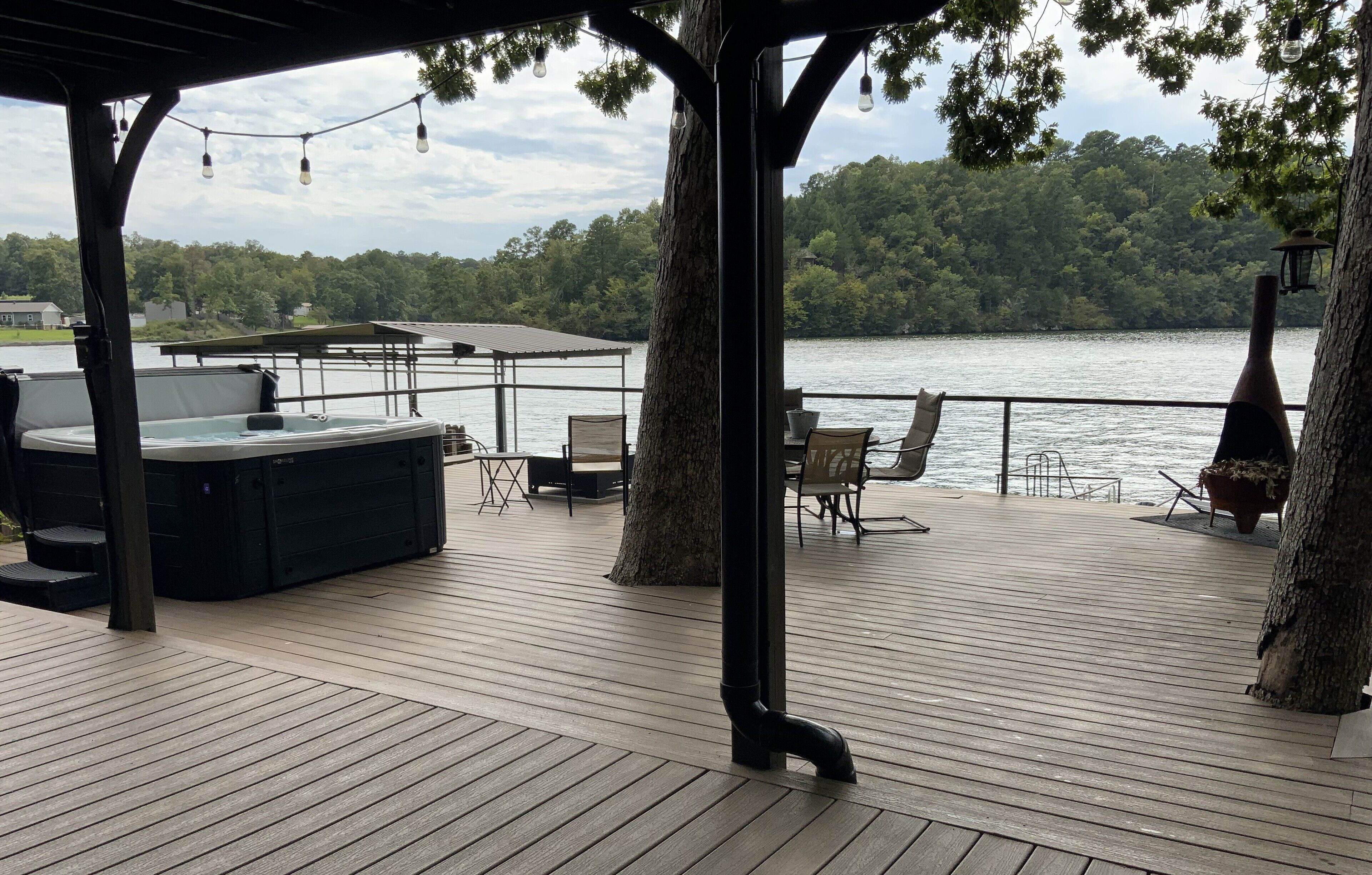 A wooden deck with a hot tub, chairs, and a pergola with string lights.