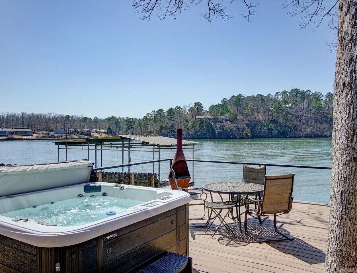 A hot tub on a wooden deck with a view of a lake and trees.