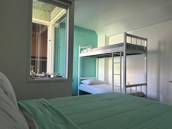 Una habitación con una litera, una cama individual y un ventanal con vistas al verdor.