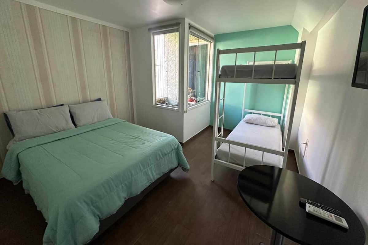 A room with a bunk bed, a single bed, a small table, and a window with a view.