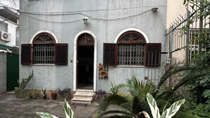 Un edificio de dos pisos con ventanas arqueadas y contraventanas, una pequeña entrada y plantas en macetas al frente.