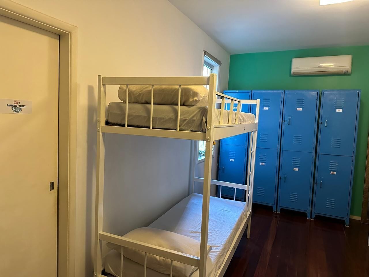 Una cama litera con ventana, una puerta y taquillas azules al fondo.