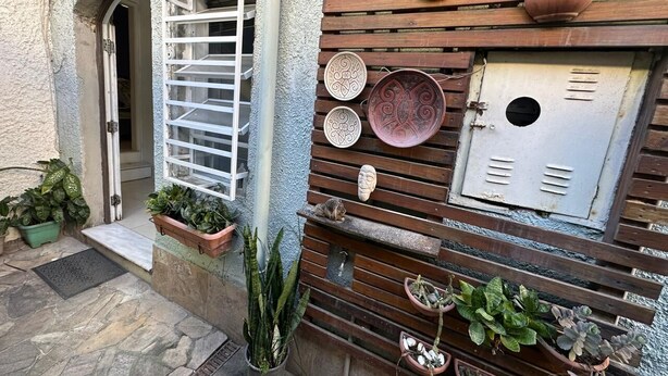 Un edificio rústico con un muro de listones de madera, una puerta metálica y diversas plantas en macetas.