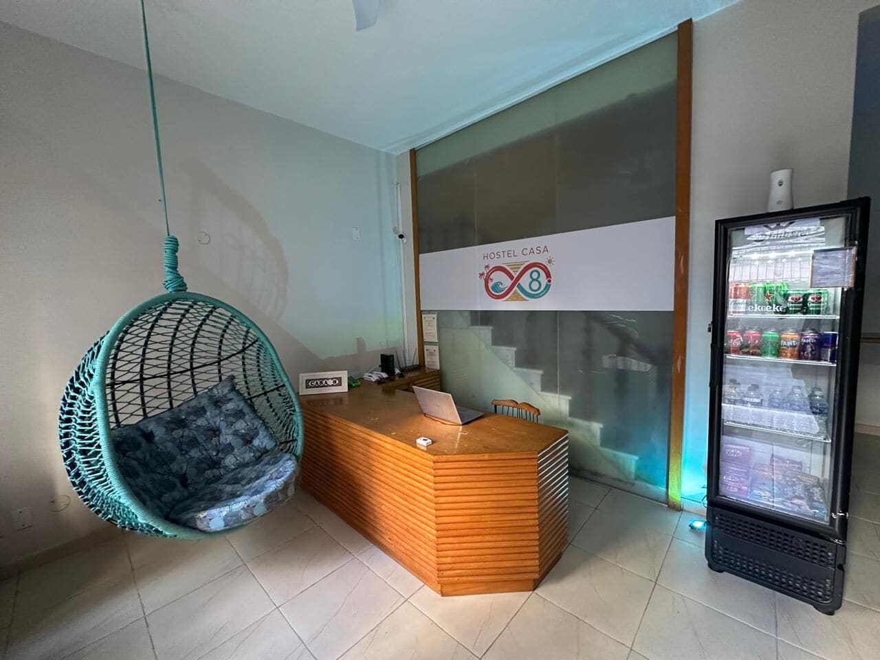 A reception area with a wooden reception desk, a hanging chair, a glass partition, and a beverage refrigerator.