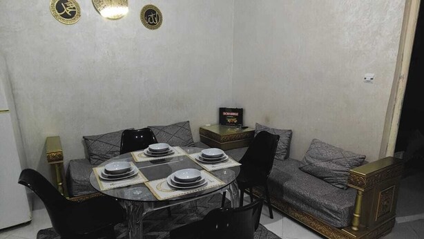 A dining area with a round table set for four, surrounded by black chairs. There is a sofa with a patterned throw and a decorative box on a side table. - Apartment in the heart of Oran, near the seafront (Oran)