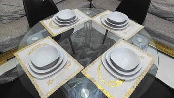 A round glass table with four white plates and matching placemats, set against a grey sofa and a small side table with a Scrabble box.