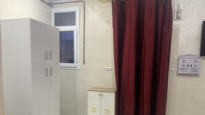 A small, clean room with a white wardrobe, a small cabinet with a logo, a window, and a door with a curtain. - Apartment in the heart of Oran, near the seafront (Oran)