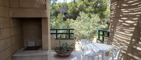 A patio with a table and chairs, a potted plant, and a view of trees and greenery.