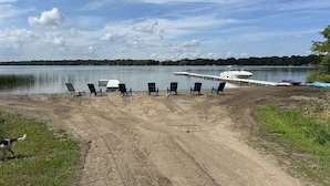 A lakeside view with a dock, chairs, and a boat.