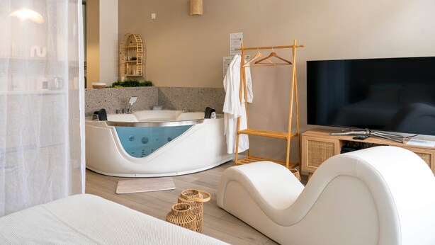 A modern bathroom with a bathtub, a television, and a seating area. - Sensual suite and balneotherapy (Nemours)