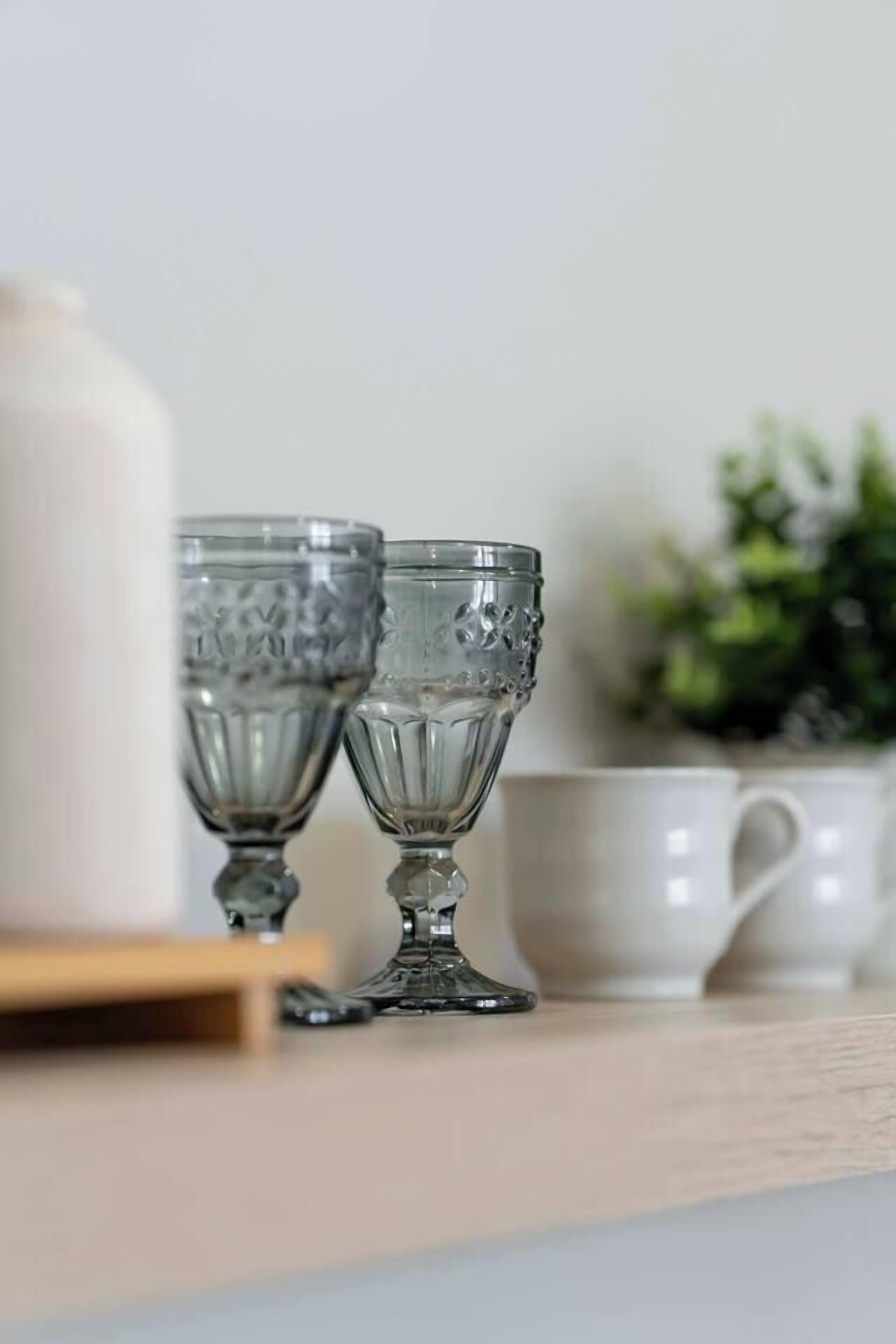 Two clear glass cups on a wooden surface with a white mug in the background.