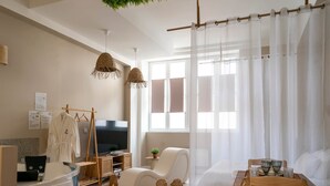 A modern hotel room with a large window, a TV, a sofa, a wooden table, and a reception desk. - Sensual suite and balneotherapy (Nemours)
