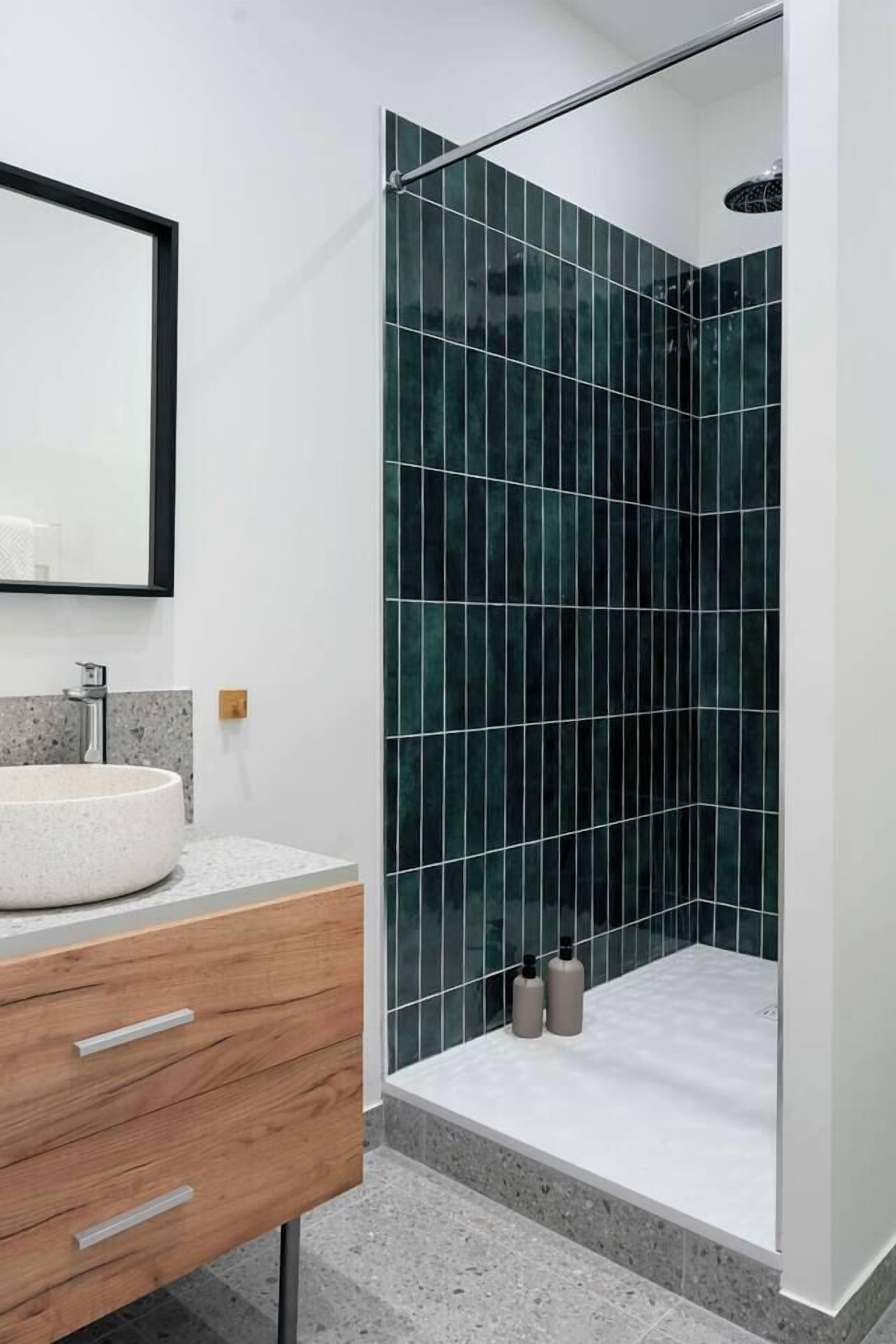 A modern bathroom with a freestanding sink, a mirror, and a shower with dark green tiles.