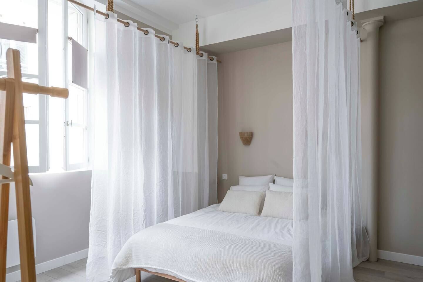 Un dormitorio con cama a dosel, un caballete de madera y una lámpara fijada a la pared.