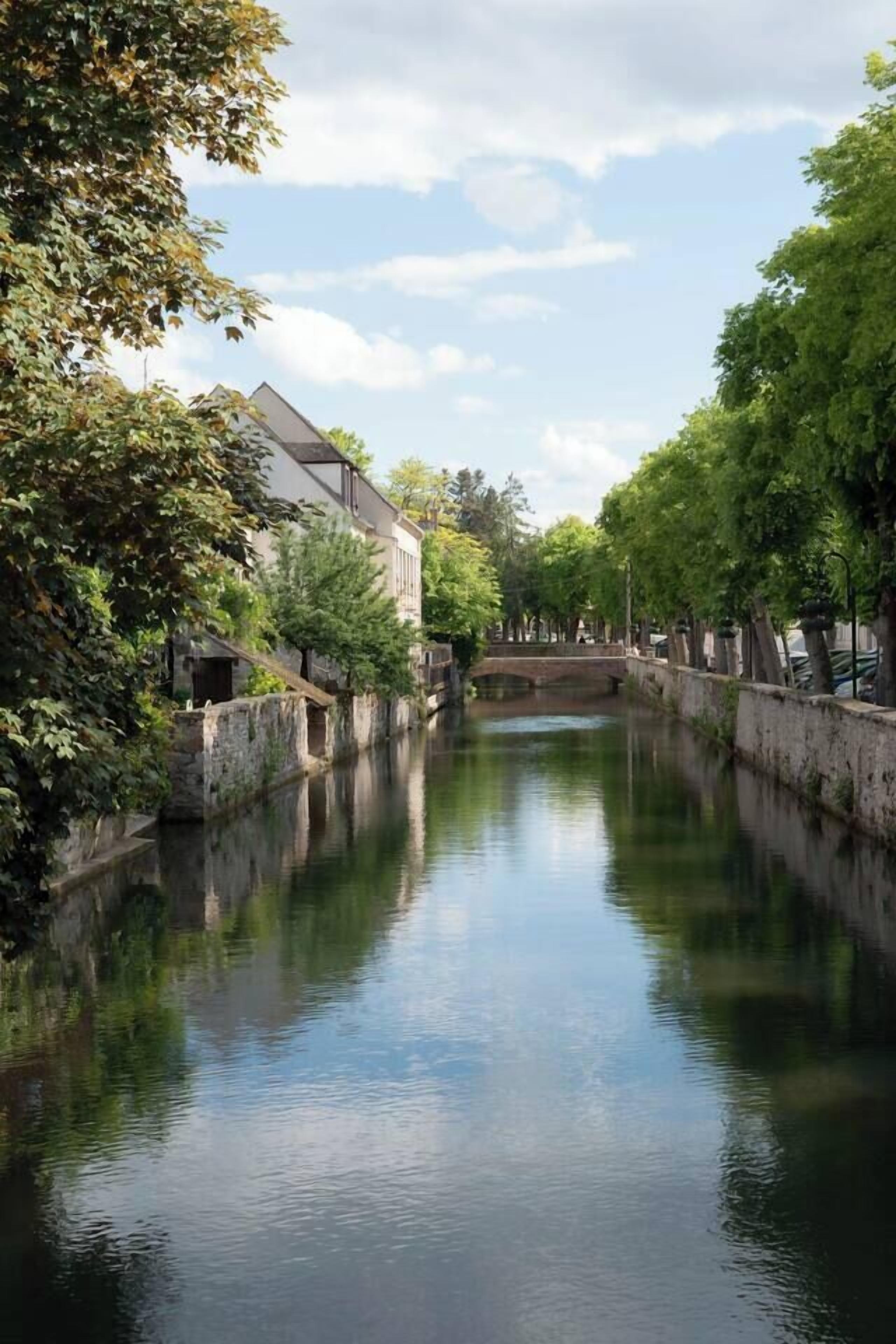 Un río tranquilo con un puente de piedra, rodeado de árboles y edificios.