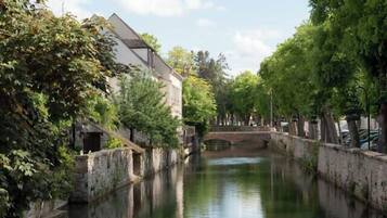 Un río tranquilo con un puente de piedra, rodeado de árboles y edificios.