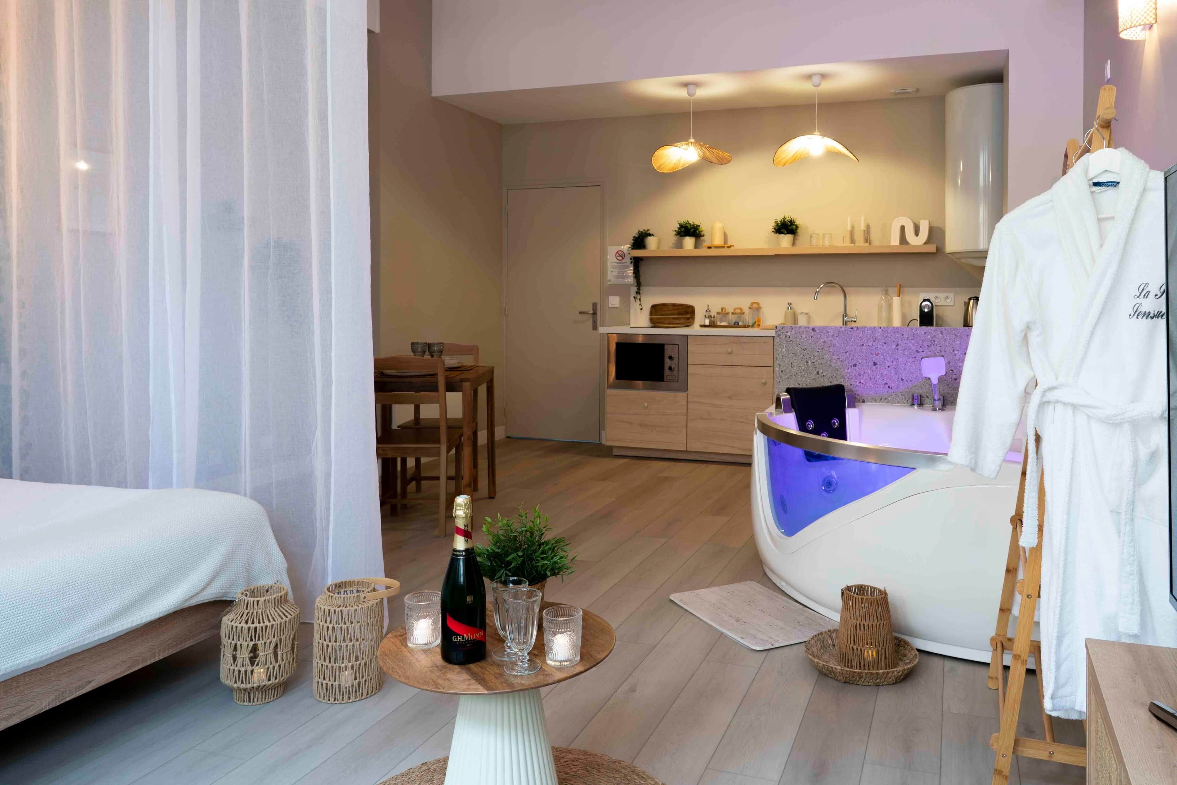 Ein modernes Hotelzimmer mit Bett, einer kleinen Essecke, einer Küchenzeile und einem Wellnessbereich mit Badewanne.