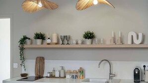A modern kitchen with two hanging pendant lights, a wooden shelf with decorative items, and a built-in sink. - Sensual suite and balneotherapy (Nemours)