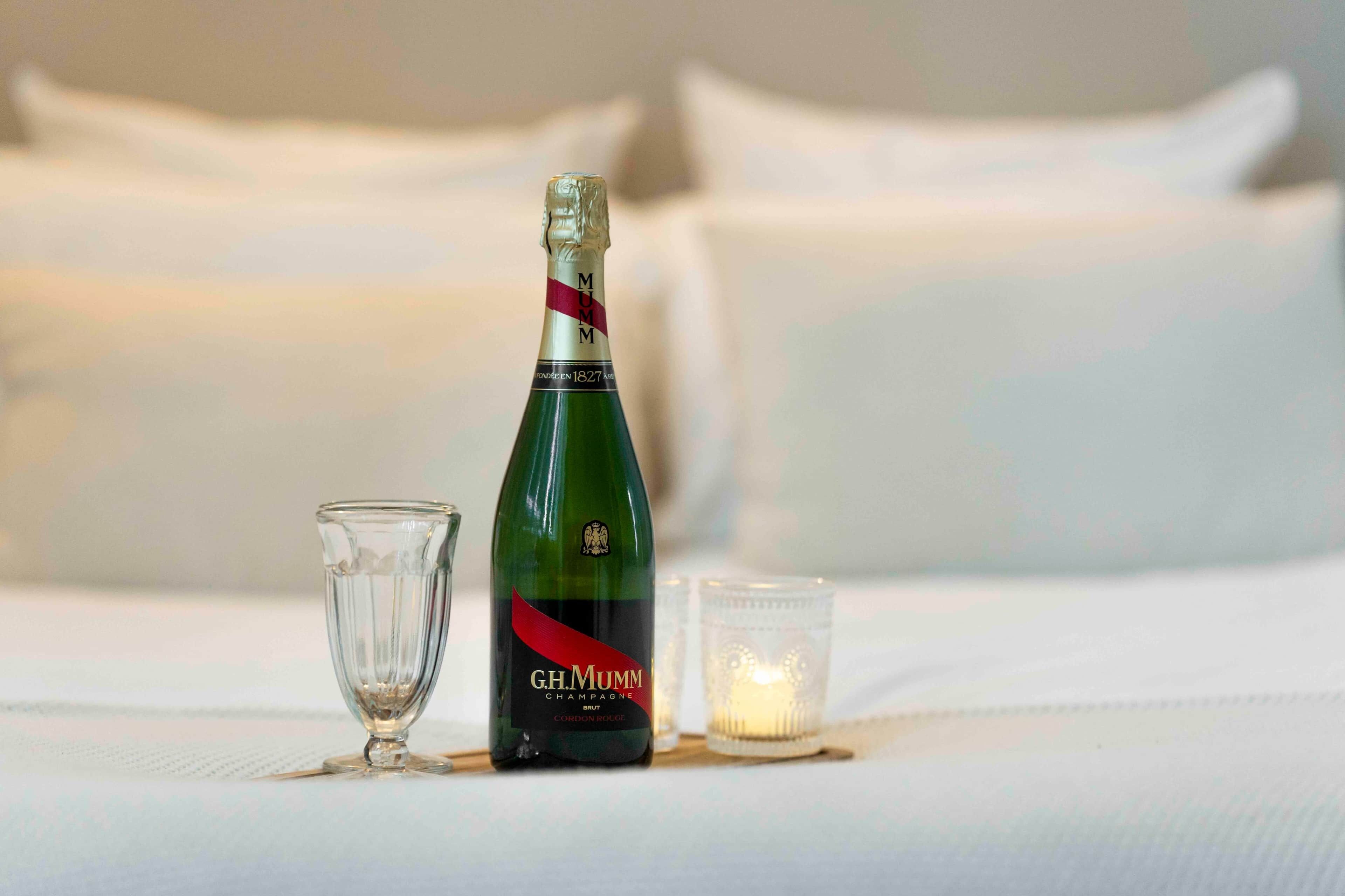 Une bouteille de champagne G.H. Mumm, un verre et une bougie sur un lit.