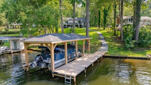 A docked boat with a covered structure, surrounded by lush greenery and a well-maintained lawn. - Lakefront 4BR, Hot Tub, Kayaks, Paddleboards, Fire pit, Fireplace, Pool Table (Littleton)