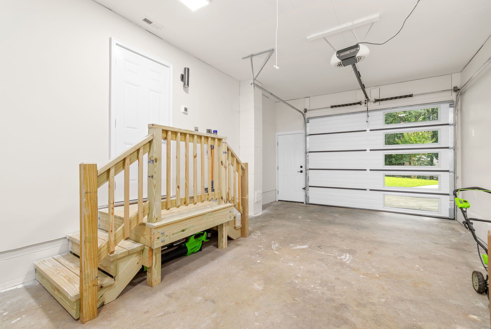 Eine Garage mit einer Holztreppe, einer weißen Tür und einer Garagentür mit Fenstern.