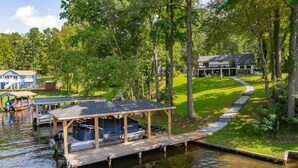 A lakeside property with a dock, a covered boat house, and a house with a large deck. - Lakefront 4BR, Hot Tub, Kayaks, Paddleboards, Fire pit, Fireplace, Pool Table (Littleton)