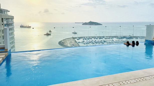 An infinity pool with a view of the sea, boats, and a distant island. - Blue Loft 14th floor, Jacuzzi, Sauna, Turkish bath, swimming pool, gym, spa, bar. (Santa Marta)