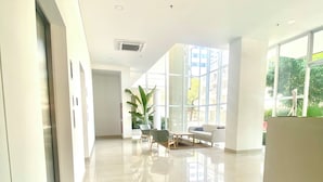 A spacious, well-lit hallway with a modern design, featuring a large window, a seating area with a sofa and chairs, and a plant. - Blue Loft 14th floor, Jacuzzi, Sauna, Turkish bath, swimming pool, gym, spa, bar. (Santa Marta)
