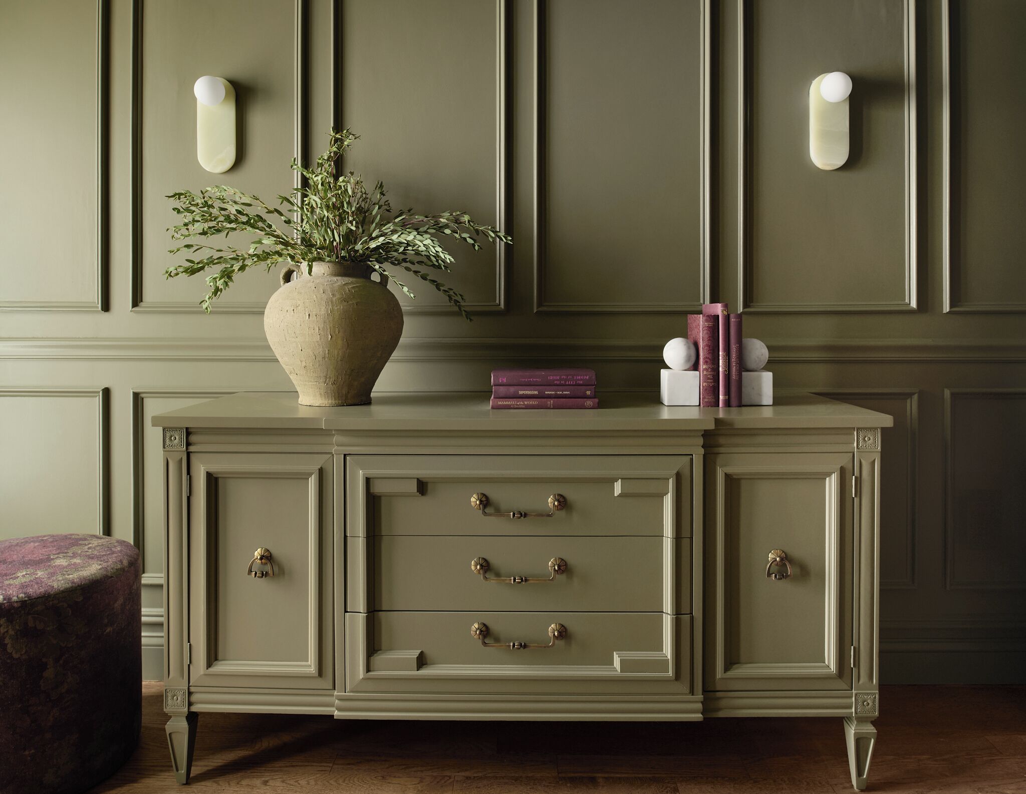 A green upholstered cabinet with drawers and a vase with green foliage.
