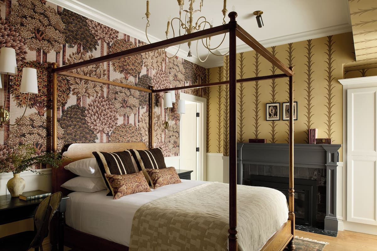 A four-poster bed with a canopy, a fireplace, and a patterned wallpaper.