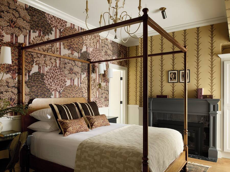 Un lit à baldaquin, une cheminée et un papier peint à motifs.