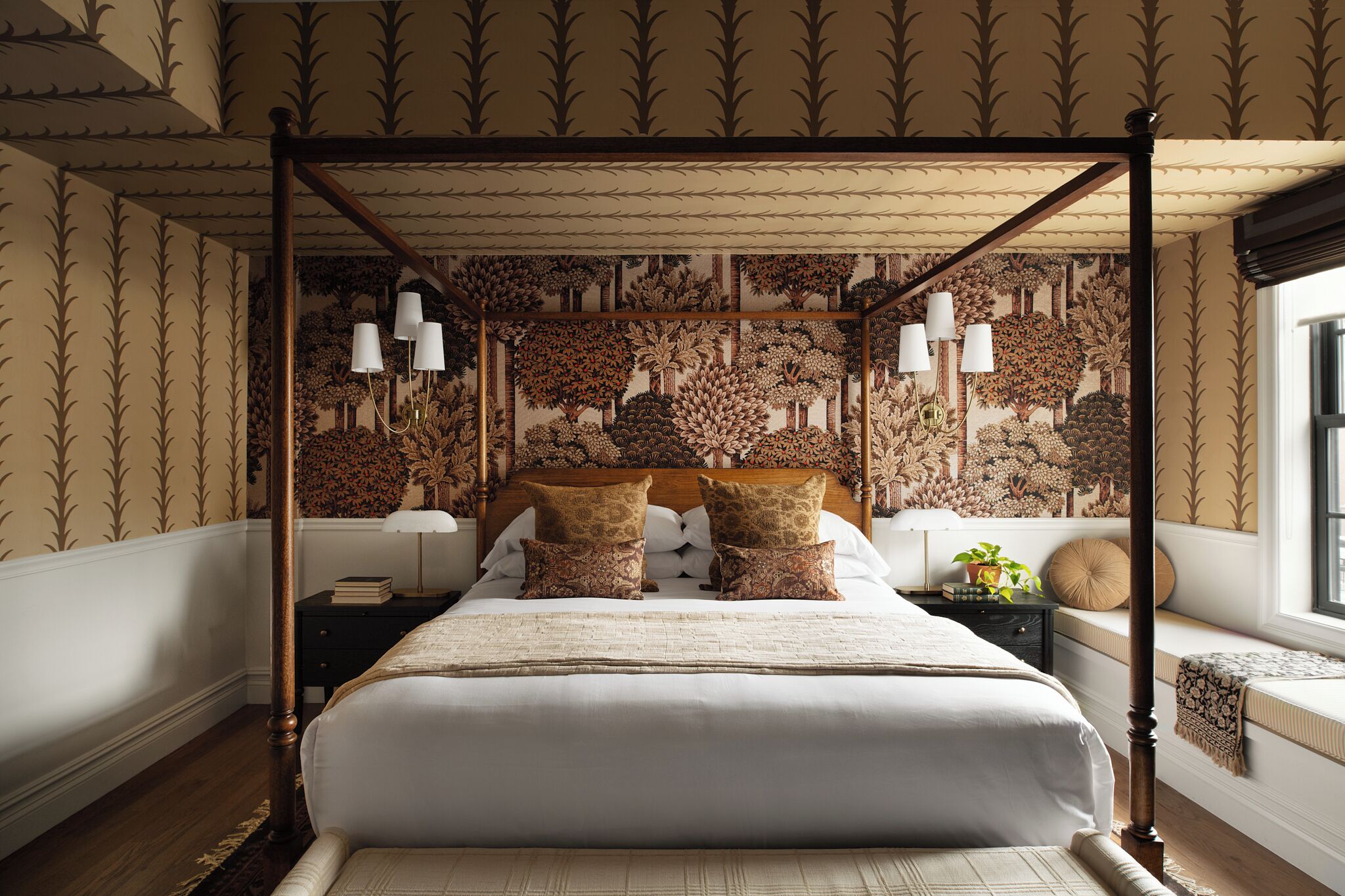 Ein Himmelsbett mit gemustertem Wandpapier, Nachttische und ein Fenster mit Blick.